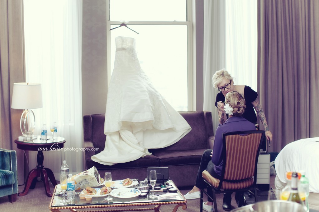 Picture of bride getting her makeup done with dress in background. Ann Louise Photography