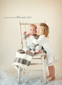 Portrait of little girl kissing baby boy sitting in chair by Kelly Klatt Photography