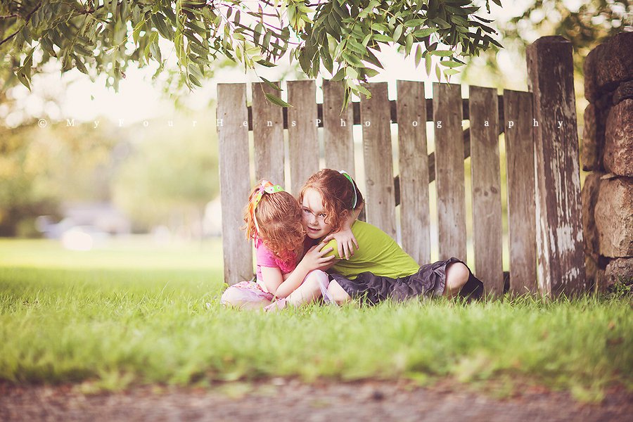 Portrait of sisters hugging outside in front of fence by My Four Hens Photography